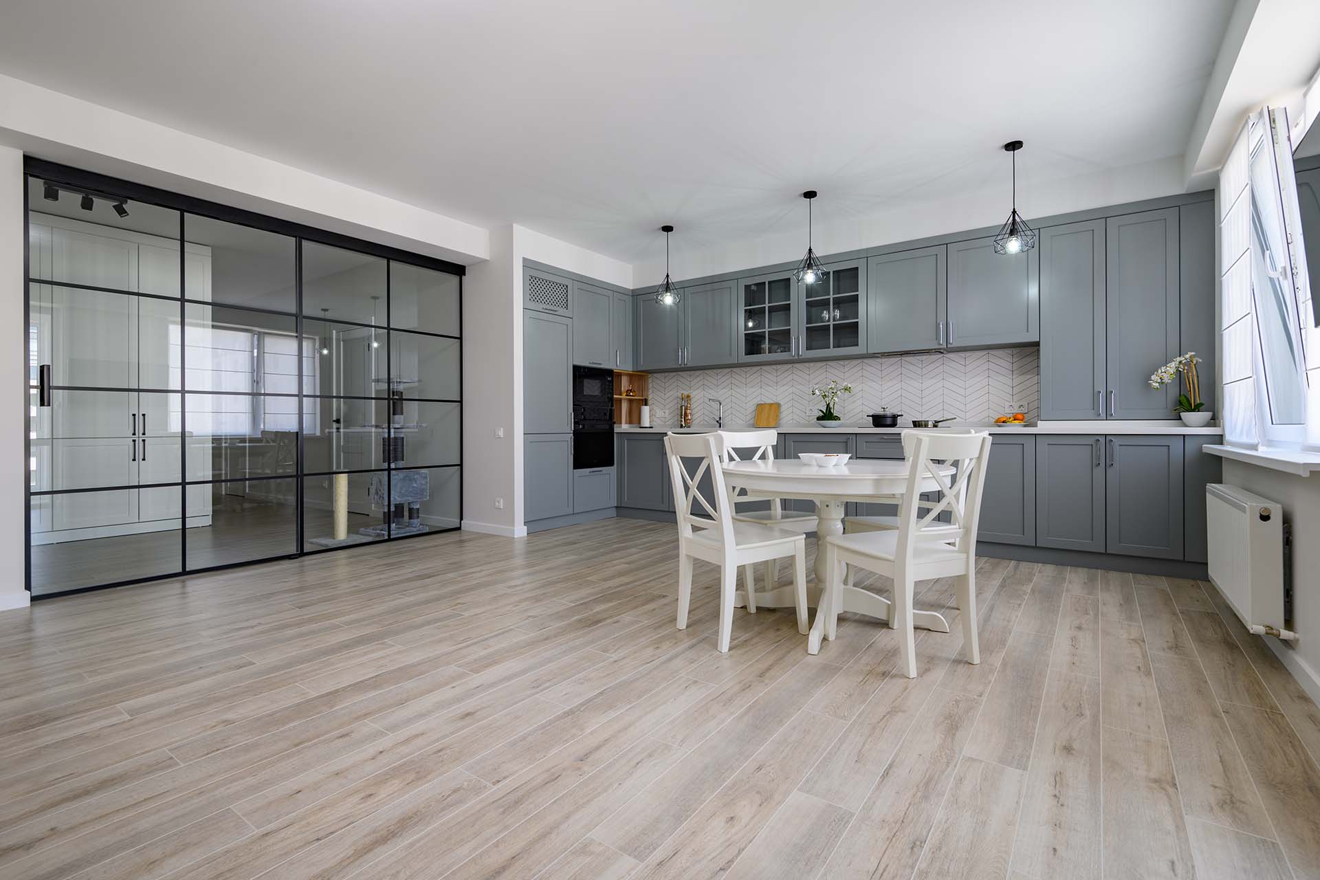 Trendy grey and white modern kitchen furniture in studio apartment and laminate wood flooring.