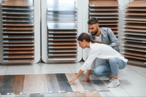 A couple choosing parquet flooring with rows of different floor sheets displayed behind them.