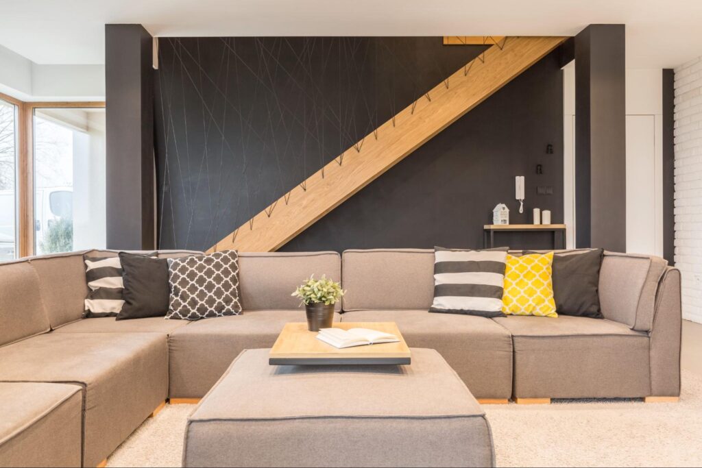 Brown-themed sofa with designer throw pillows in a newly remodeled basement featuring a gray accent wall that adds a modern touch.