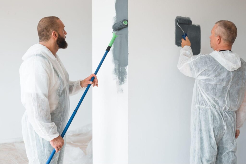 Two professional painters in protective suits paint the walls of a newly built apartment.