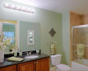 Well-furnished bathroom in pastel green and blue hues, featuring a large white vase with artificial flowers on the sink and light green towels neatly displayed.