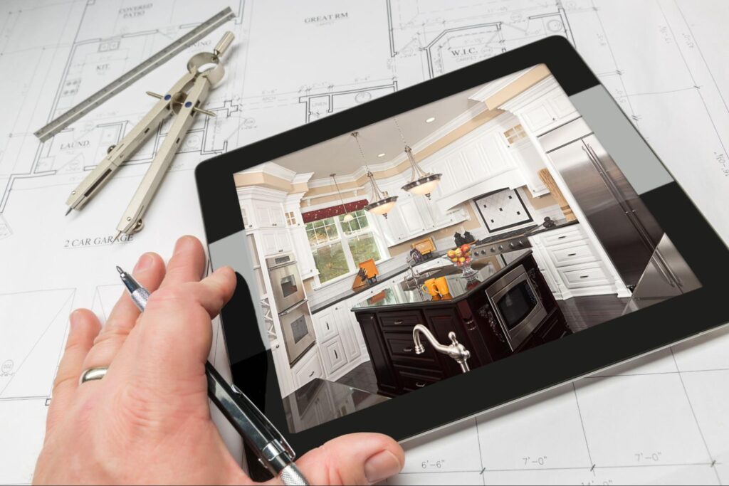 A close-up of an architect's hand on top of a table showing a photo of a kitchen with a blueprint.