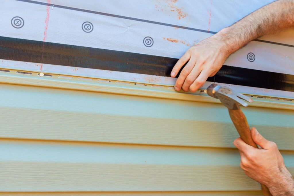 Man using a hammer to install siding on a home.