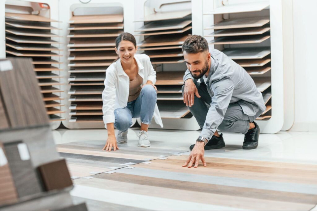 Man and a woman looking at flooring samples while crouched down on the floor.