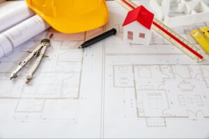 Blueprint next to a hard hat, tools, and a model of a home