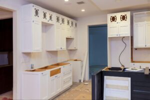 A kitchen under construction with newly installed white cabinets and a wire exposed.